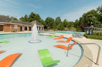 A swimming pool with a fountain and orange and green chairs