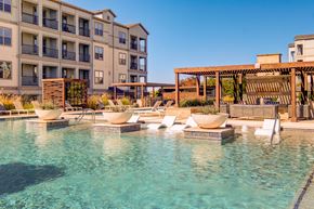 Rowlett apartment for rent - A pool area with lounge chairs and a building in the background.