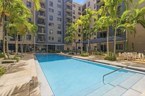 Miami apartment for rent - A swimming pool surrounded by palm trees and apartment buildings.