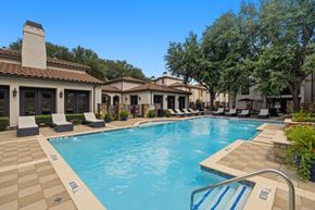 Dallas apartment for rent - A large swimming pool surrounded by lounge chairs and trees.