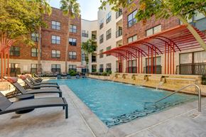 Houston apartment for rent - A pool surrounded by lounge chairs and a red awning.
