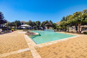 Austin apartment for rent - A large outdoor swimming pool surrounded by a brick patio and lounge chairs.