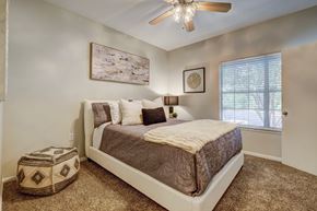 Austin apartment for rent - A bedroom with a bed, pillows, a ceiling fan, and a window.