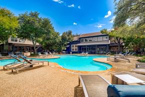 Austin apartment for rent - A large outdoor swimming pool surrounded by lounge chairs and trees.