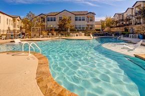 Lakeway apartment for rent - A large swimming pool with a sandy edge and a residential building in the background.