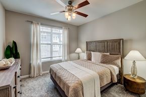 Atlanta apartment for rent - A bedroom with a large bed, a ceiling fan, and a window with curtains.