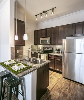 Conroe apartment for rent - A kitchen with a stainless steel refrigerator and dark brown cabinets.