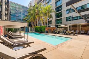 Los Angeles apartment for rent - A pool surrounded by chairs and a building in the background.