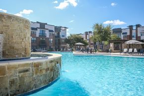 Mckinney apartment for rent - A swimming pool with a stone wall and a building in the background.