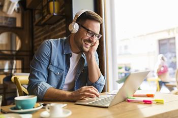 A man in a denim shirt is using a laptop and wearing headphones.