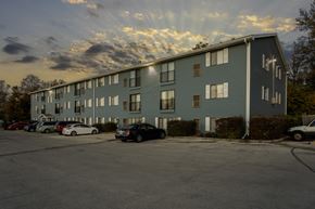 Des Moines apartment for rent - A parking lot in front of a grey apartment building with cars parked.