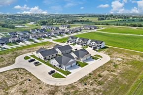 Van Meter townhouse for rent - A large, modern house with a driveway and several cars is surrounded by smaller houses in a rural setting.