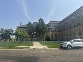 Miles City apartment for rent - A white car is parked in front of The Cornerstne Apartments with a fence and trees.
