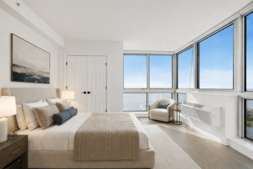 Jersey City apartment for rent - A bedroom with a large bed and a view of the sky through the windows.