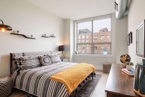 Jersey City apartment for rent - A bedroom with a bed and a window overlooking a city.