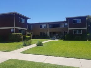 Los Angeles apartment for rent - A building with a brown and beige exterior is surrounded by a green lawn and a clear blue sky.