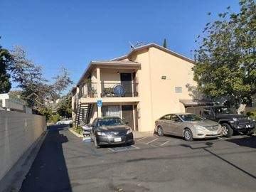 Los Angeles apartment for rent - A car is parked in front of a building with a blue sign on it.