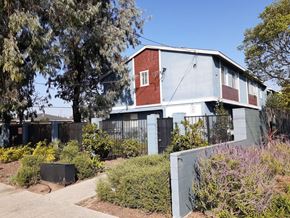 Los Angeles apartment for rent - A red and white house with a grey fence and green bushes in front.