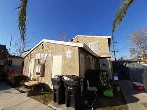 Los Angeles apartment for rent - A house with a brown wall and a white door is surrounded by a fence and has a green lawn.
