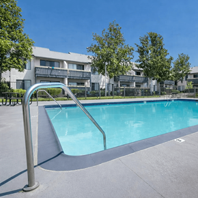 San Bernardino apartment for rent - A swimming pool with a ladder in the foreground and apartment buildings in the background.