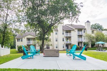 A fire pit and lounge chairs sit on a concrete patio in front of an apartment building