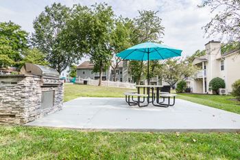 A patio with a table and umbrella and a grill