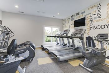 A gym with four treadmills and a television