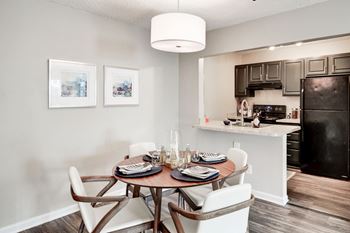 A dining area with a table and chairs and a kitchen in the background