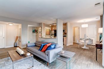 A living room with a couch table and chairs and a kitchen in the background