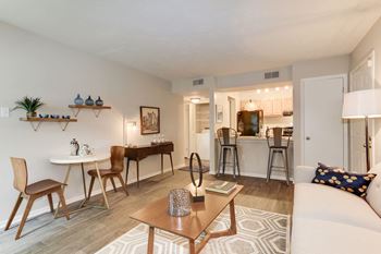 A living room with a couch a table and a chair and a kitchen in the background