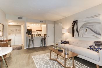 A living room with a couch coffee table and a kitchen in the background