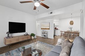Chandler apartment for rent - A living room with a grey sofa, a wooden coffee table, a flat screen TV, and a ceiling fan at Riviera Park, Chandler Arizona