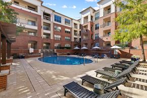 Farmers Branch apartment for rent - A large outdoor pool area with sun loungers and umbrellas in front of apartment buildings at Prairie Crossing, Farmers Branch, Texas