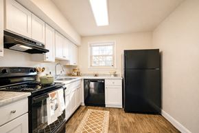 Capitol Heights apartment for rent - A black refrigerator stands in a kitchen with white cabinets and a black stove ighland Ridge Apartments, Capitol Heights, MD, 20743