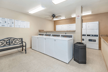 A room with a bench, a trash can, and a wall with a list of items on it.