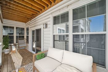 A white couch is on a wooden deck with a table and chairs