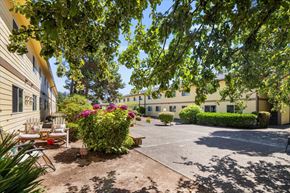 Lincoln City apartment for rent - A sunny day at a residential complex with a parking lot and greenery.