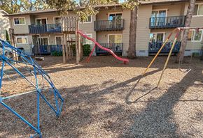 Beaverton apartment for rent - A playground with a blue swing set and a red slide in front of apartment buildings.