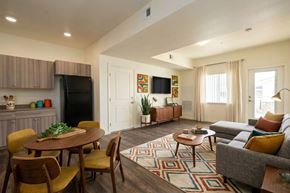 Gridley apartment for rent - A living room with a grey couch, a wooden table and chairs, a black fridge, a flat screen TV, and a rug.