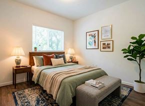 Gridley apartment for rent - A bedroom with a bed, two lamps, a bench, and a potted plant.