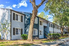 Jacksonville apartment for rent - A tree stands in front of a two-story building with blue siding.