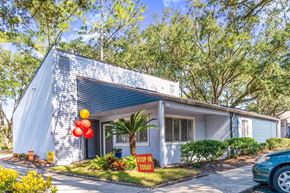 Jacksonville apartment for rent - A house with a blue roof and a sign that says "STOP IN TODAY" is surrounded by trees and has a car parked in front.