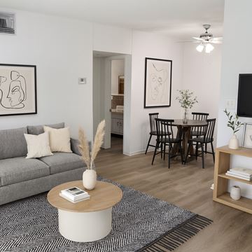 Boca Raton apartment for rent - A living room with a grey sofa, a coffee table, a dining table with chairs, and a TV on the wall.