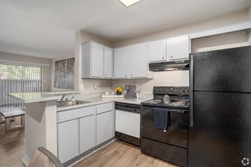 Houston apartment for rent - A black fridge sits in a kitchen with white cabinets and a black stove.