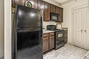 San Antonio apartment for rent - A black refrigerator stands in a kitchen with wooden cabinets and a tiled floor.
