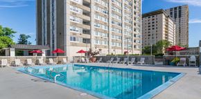 Hackensack apartment for rent - a swimming pool with chaise lounge chairs and umbrellas in front of a tall building at The Ivanhoe Apartments, Hackensack, NJ