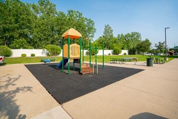 Maple Grove apartment for rent - A playground with a yellow and green structure in the middle of a paved area.
