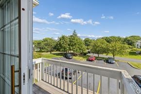 Rochester apartment for rent - A view from a balcony looking out at a parking lot and trees.