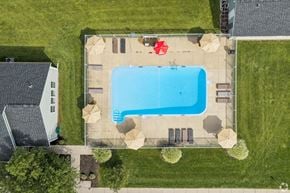 Farmington townhouse for rent - A large swimming pool surrounded by a concrete patio and a small white house.