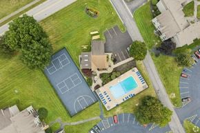 Fairport townhouse for rent - A tennis court is surrounded by a parking lot and a pool.